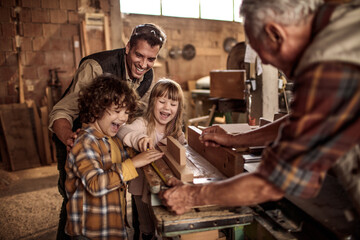 Cute little children working with older carpenters in workshop - obrazy, fototapety, plakaty