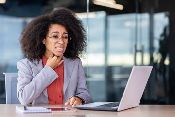 Unhappy African American businesswoman suffering from sore throat and coughing, holding hand on neck, working in office.