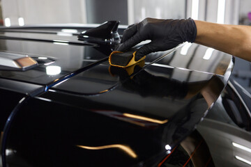 The process of applying a nano-ceramic coating on the white car's hood by a male worker in blue...