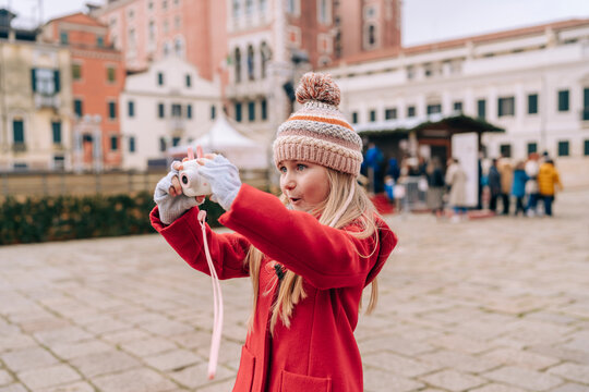 Intent and focused, a young girl with a camera takes a picture, immersed in the cultural backdrop of a Venetian square