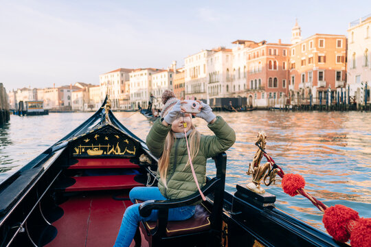 A girl captures her Venetian gondola experience with a toy camera, historic buildings line the Grand Canal in the golden hour