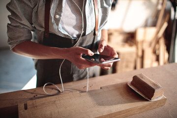 Close up female carpenter using smartphone in wood workshop