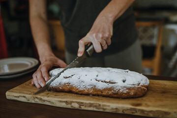 Women's hands cutting fruitcake on board with knife.