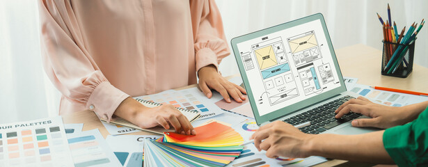 Cropped image of interior designer chooses color from color swatches while laptop displayed website...