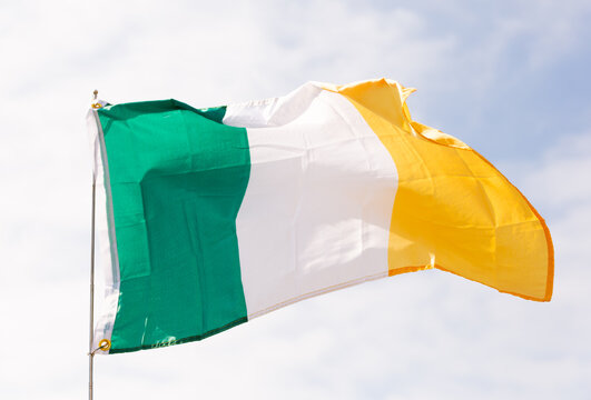 Big flag of Ireland fastened on stick against background of blue cloudy sky under daylight