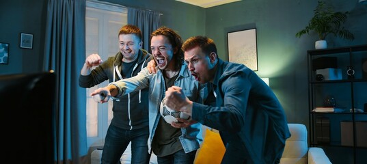 Happy Caucasian male football fans friends standing in front of TV screen in dark living room on...