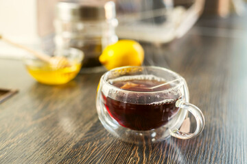 Cup of hot black tea, bowl with honey and lemon on a wooden table
