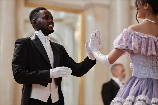 Waist up portrait of young Black gentleman dancing with lady hand to hand in palace ballroom, copy space