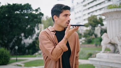 Young man recording voice message nature background. Hispanic guy talking cell