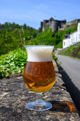 Glass of blond strong Belgian abbey beer on old castle wall in sunny day with nice view on old town Bouillon, Belgium