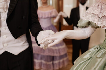 Close up of unrecognizable lady and gentleman holding hands wearing gloves entering ballroom together, copy space