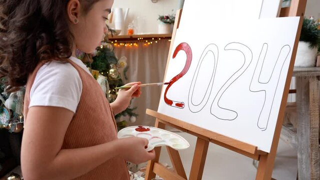 Little talented cute girl artist painting on drawing easel with canvas palette and brush the red numbers 2024. Happy new year 2024. Art school.