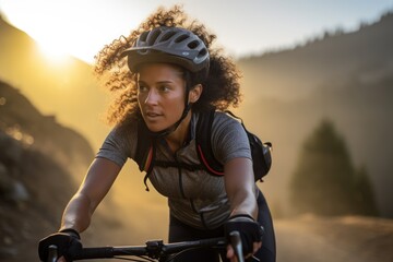 athletic young woman is mountain biking on a rugged trail at sunset, with warm light illuminating her focused expression and curly hair