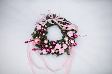 Pink Christmas tree toys on a wreath of fir branches on a table with snow
