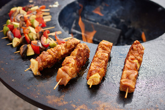 Round grill in the shape of a bowl with fire inside. A man prepares a hearth for barbecue. The round hearth is cleaned before cooking. The firewood lies in the bowl of the outdoor hearth.