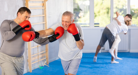 Two men in group boxing classes practicing sparring technique of blowing to head in gym
