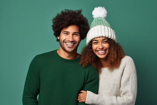 Merry young cheerful smiling couple two friends man woman wear sweater hold in hand pompom of Santa hat posing isolated on plain green background. Happy New Year celebration Christ