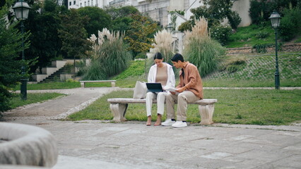 College students learning tablet on bench. Business couple working in green park