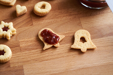 Filling a bell shaped Linzer Christmas cookie with strawberry marmalade
