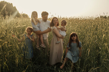 Family portrait on a field in rye in the rays of the setting sun. Father and mother hug their...