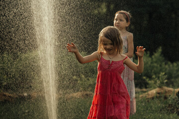 Girls play in the garden in summer, splash with water, have fun