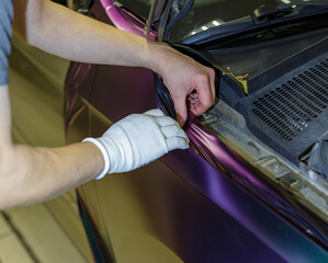 A specialist in wrapping a car with chameleon-colored vinyl film in the process of work. Car wrapping specialists cover the car with vinyl sheet or film. Car wrapping close-up. Selective focus.
