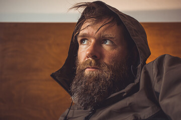 Weird bearded man on a brown wooden background, wearing a hoodie or softshell. Retro image of a...