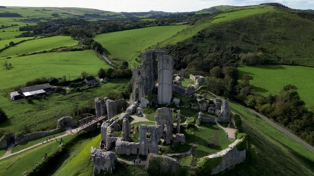Aerial shot ruins of Corfe Castle on hill with scenery passing in the background on autumn day. Top cinematic aerial view. United Kingdom aerial. 