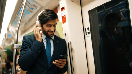 Smart executive manager wear headphone and listen music while standing in train. Professional...