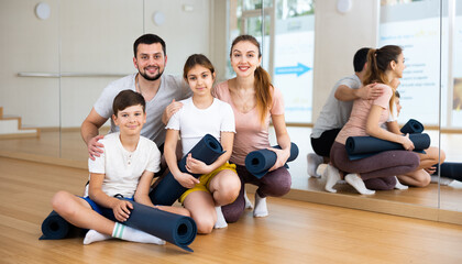 Fototapeta premium Smiling fit woman and man with teenage girl and boy posing with yoga mats before training in modern gym..