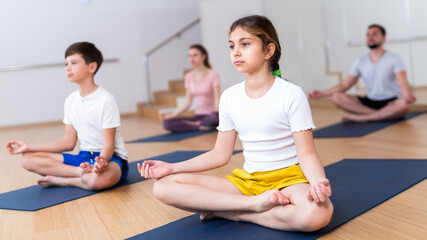 Portrait of focused tween girl practicing yoga asanas with family at yoga studio