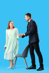 Obraz premium Young man offering his wife to sit in chair on blue background