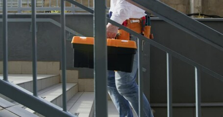 Man going up stairs on way to work. Worker laden with toolbox and trusty tool-belt walks up stairs with purpose ready to dive into working day