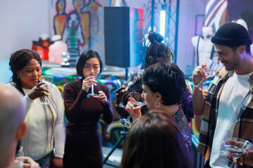 Diverse people crowd drinking alcohol beverages while celebrating in nightclub. Youn friends group holding glasses while socializing and partying on dancefloor at social gathering