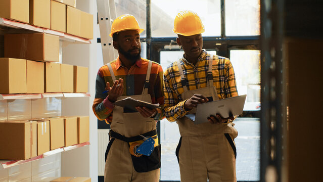 Team of men checking supplies and cargo in depot, using laptop and inventory list in storage room. Workers organizing stock with cardboard boxes on shelves, check merchandise in warehouse.