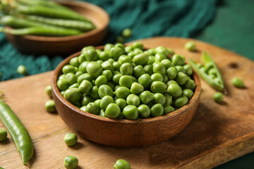 Bowl and wooden board with fresh green peas on color background, closeup