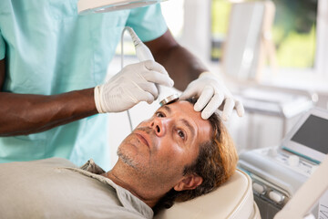 Adult male patient receiving facial procedure with high frequency ultrasonic vibration attachment...