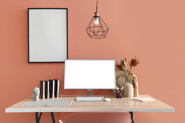 Modern computer, stationery and decor on wooden table near color wall