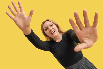 Scared mature woman on yellow background