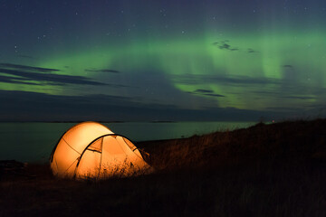 Northern lights dancing over an iluminated tent at the Atlantic coast in Norway