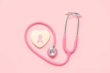 Heart shaped cookie with ribbon and pink stethoscope on color background. Breast cancer awareness...