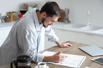 Young man reading newspaper in kitchen