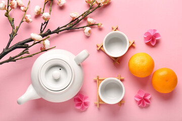 Obraz na płótnie Canvas Teapot with cups, mandarins and sakura on pink background. Japanese New Year celebration