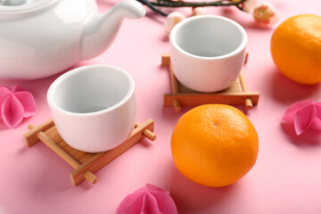 Teapot with cups, mandarins and sakura on pink background. Japanese New Year celebration
