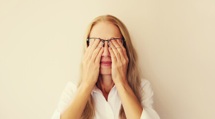 Tired overworked middle-aged woman employee rubbing her eyes suffering from eye strain, dry eye syndrome or headaches after working at the computer for a long time. Exhausted office worker