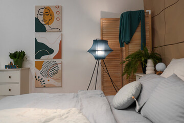 Interior of stylish bedroom with glowing lamp and paintings at night