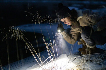 Dedicated Female Environmental Researcher Illuminating the Icy Coastline of an Alpine Lake while...