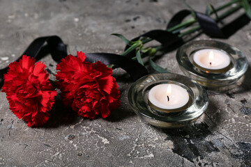 Burning candles and carnation flowers with black funeral ribbon on grunge background, closeup