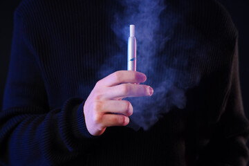 Young man with electronic cigarette on black background, closeup