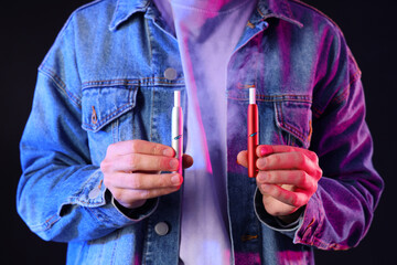 Young man with electronic cigarettes on dark background, closeup